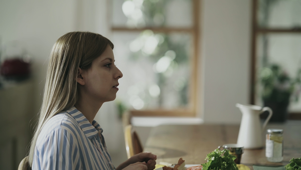 カラーグレーディングの比較画像 女性がダイニングテーブルについている、窓の外は明るいが全体的に少し暗い印象になっている